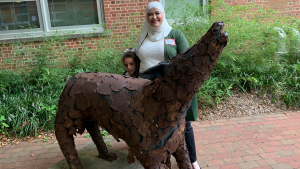 Gadeer Alzabit stands in front of an art sculpture outside.