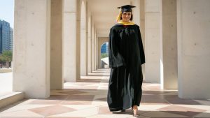 Rasha Abdullah wearing black master's regalia outside in a stone pillar hallway.