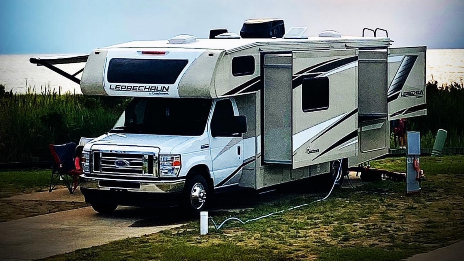 Large Ford RV parked near grass and water.