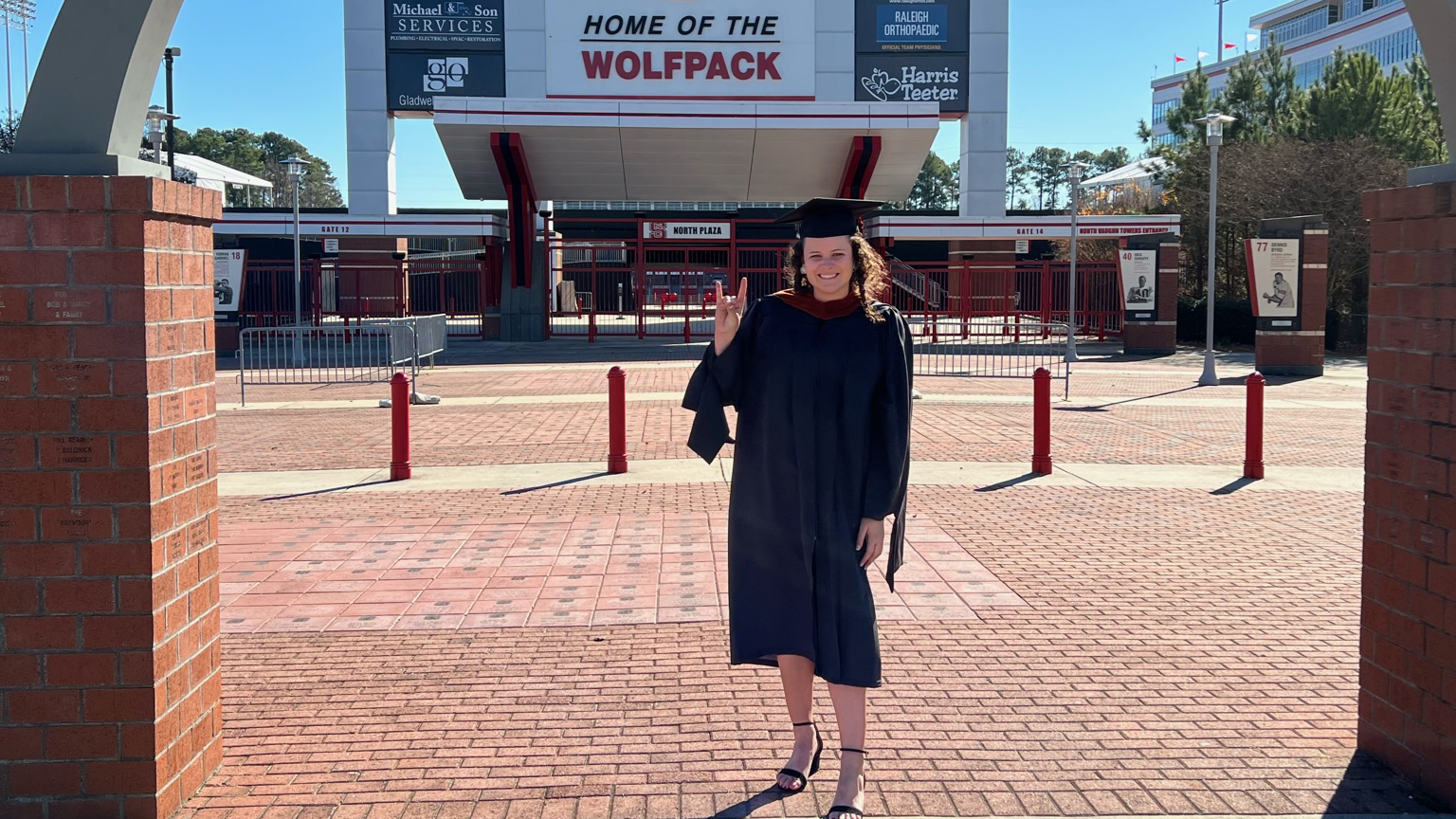Danielle Morrin stands outside of Carter-Finley Stadium on graduation day wearing her regalia.