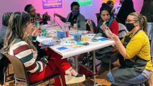 Jennifer Seaver and community members sit at an art table working on a stencil project.