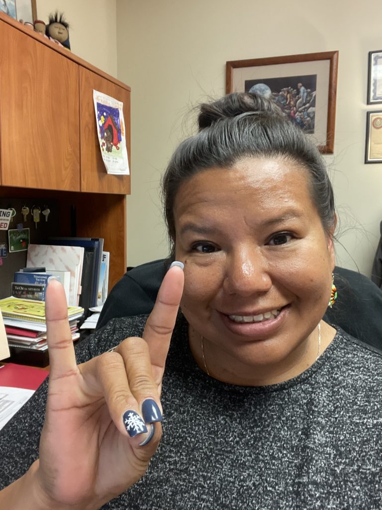 Kami Lanning at her desk making the NC State wolf hand sign. 