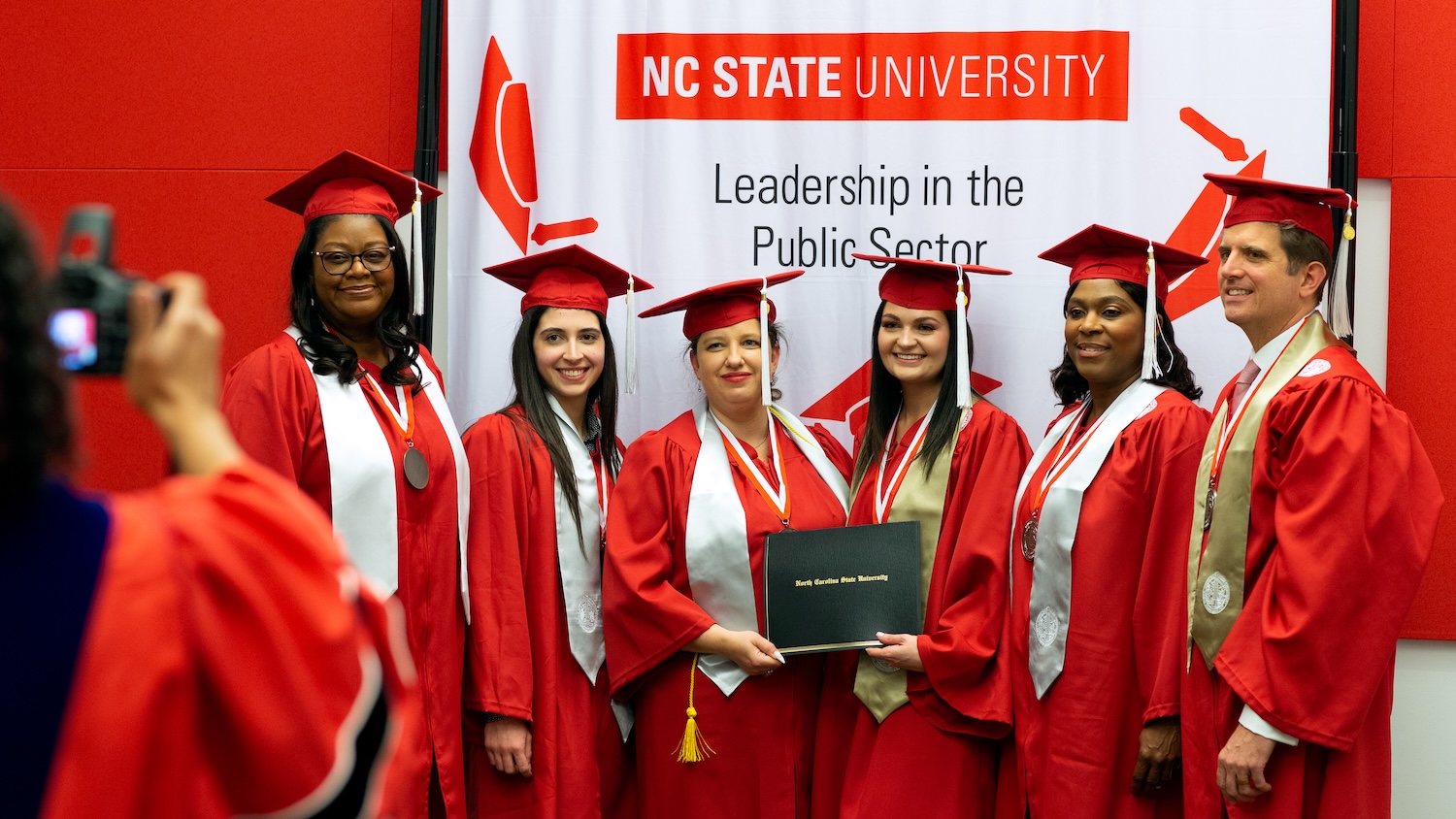 Graduates in front of an NC State University Leadership in the Public sector banner.
