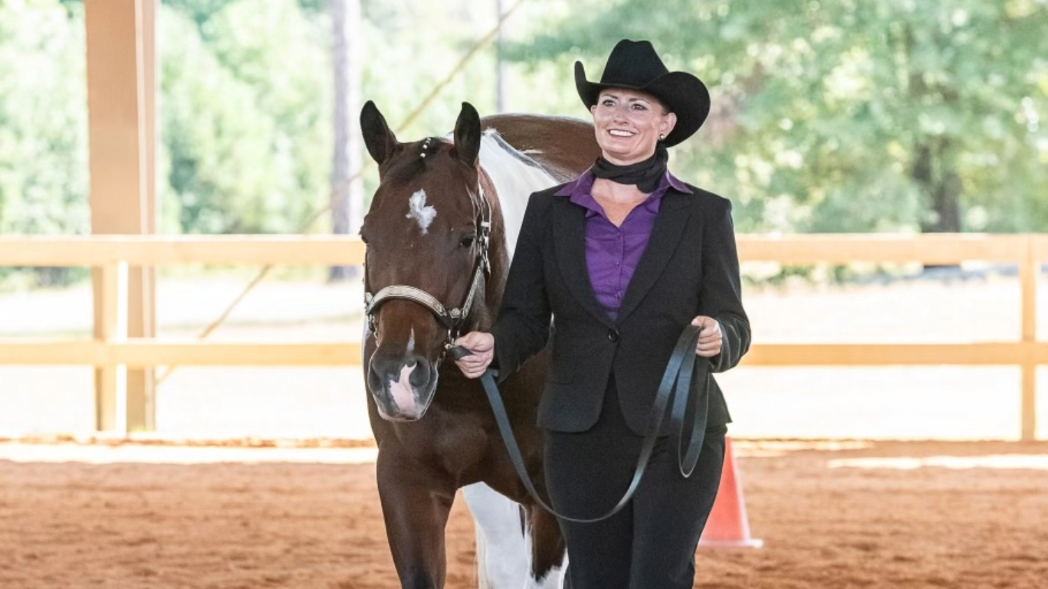 A woman in riding gear posing in a stable with a horse